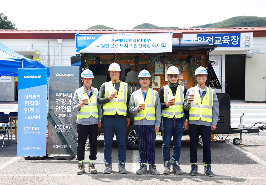 Employees of Doosan Enerbility and partner companies pose for a photo in front of the coffee truck set up at the Hamyang-Changnyeong Expressway construction